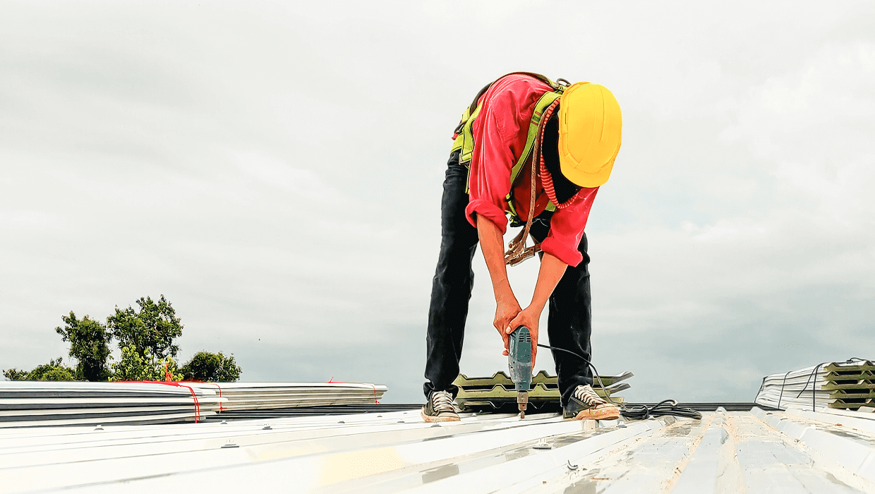 Worker installing metal roof with drill.