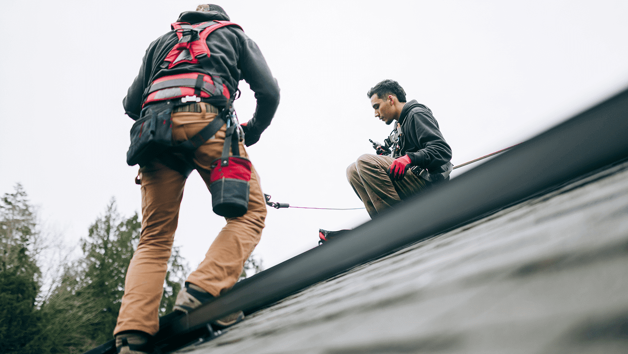 Two workers with harnesses on rooftop.
