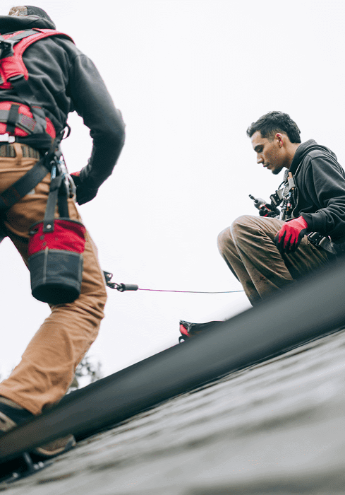 Two workers with harnesses on rooftop.